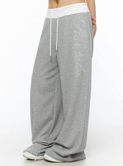 Lettering Contrast Waist Sweatpants IL515 Gray side close-up on model showing white contrast waistband, white drawstring, star-dot script graphic, and wide-leg cotton fleece texture