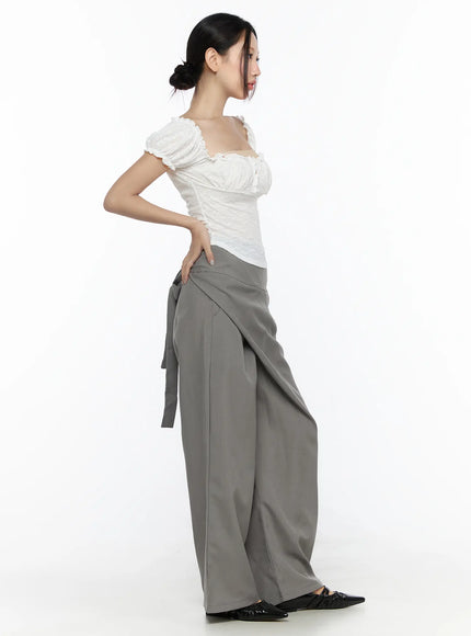 Linen Wrap Slacks CL527 Beige side profile view on model highlighting back tie bow high waistband and wide-leg drape paired with white lace crop top and black flats