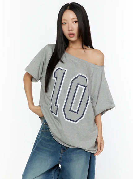 Loose Fit Oversized Tee CU526 Gray three-quarter front shot on model with hand on hip, off-shoulder fit highlighting distressed navy number 10 print and dropped short sleeve detail