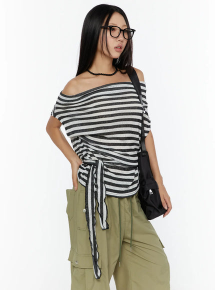 Loose Off-Shoulder Top CU526 Black angled front shot on model with glasses and bag, hand in pocket, side-tie drawstring detail, ribbed stripe