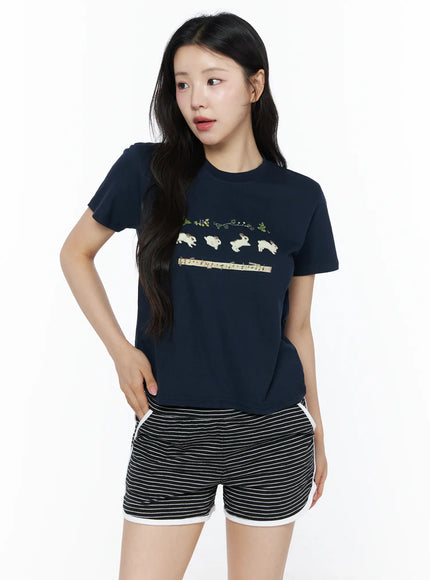 Lovely Bunny Graphic Tee IU525 Navy front shot on model hand on hip, jumping bunny botanical music note graphic on navy cropped cotton tee