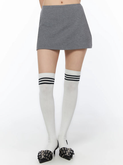 Low-Rise Mini Skort IU525 Gray front waist-down shot on model with white over-knee socks featuring navy triple stripes and black buckle heels