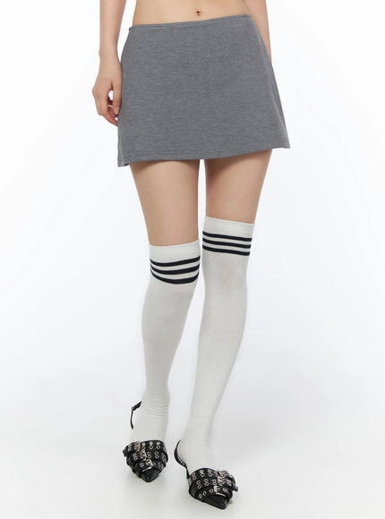 Low-Rise Mini Skort IU525 Gray waist-down front shot on model showing low-rise fit with white over-knee socks with navy triple stripes and black buckle flats