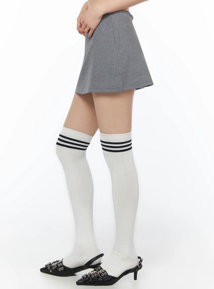 Low-Rise Mini Skort IU525 Gray side close-up on model showing A-line skort silhouette, heathered cotton texture, and white ribbed over-knee socks with kitten heels