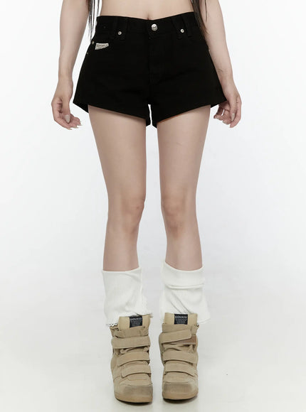 LEWKIN Low Rise Shorts IL521 Black Size S front close-up on model showing V-waistband, silver buttons, and brand patch label, styled with white leg warmers and sneakers