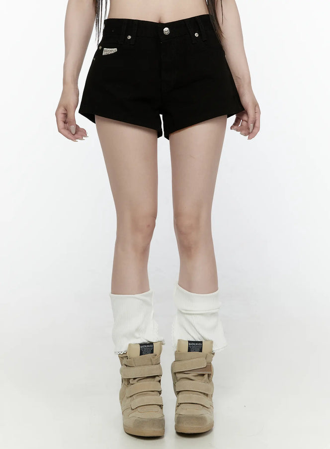 LEWKIN Low Rise Shorts IL521 Black Size S front close-up on model showing V-waistband, silver buttons, and brand patch label, styled with white leg warmers and sneakers