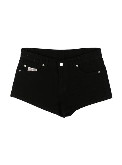 Low Rise Shorts IL521 Black flat-lay front view showing full shorts silhouette, V-waistband, silver rivets, and RUGGAS.MFG.CO brand patch on black denim