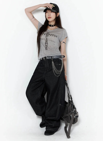 Maelani Rivet Wide Balloon Jeans IL502 Black three-quarter lifestyle shot on model in edgy outfit with cap, chain belt and bag, hand raised touching brim, dynamic pose