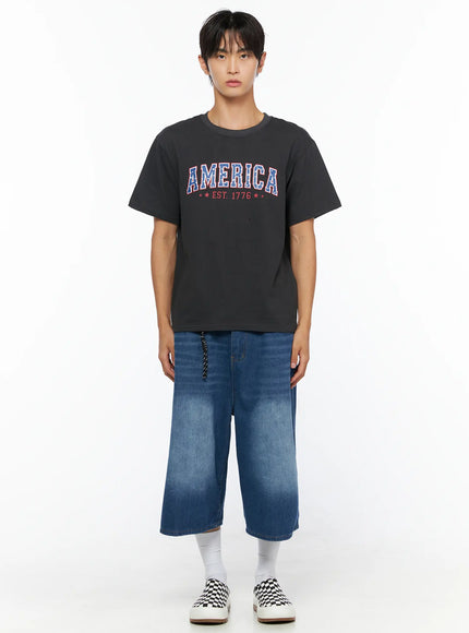 Men's America Print T-Shirt IL515 Dark gray front full-body shot on male model standing straight, AMERICA EST. 1776 graphic on cotton tee with denim shorts