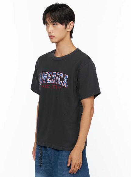 Men's America Print T-Shirt IL515 Dark gray side shot on male model showing AMERICA EST. 1776 star-print collegiate graphic and relaxed cotton silhouette