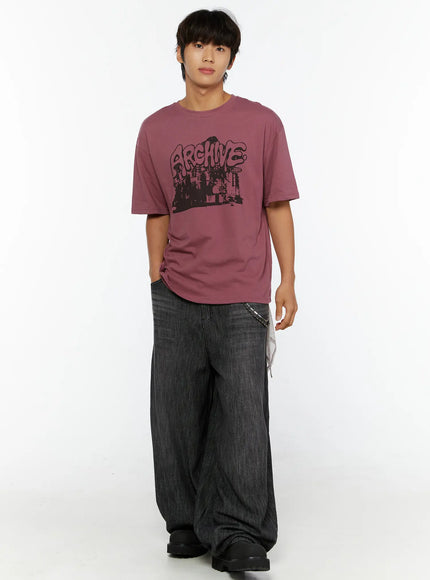 Men's Archive Graphic T-Shirt IL515 mauve full-body front view on model hand in pocket showing graffiti cityscape graphic and oversized fit with wide-leg denim