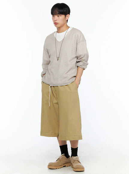 Men's Baggy Bermuda Shorts IL514 Beige three-quarter front view on model in oatmeal knit sweater turned slightly, showing drawstring waist and wide cuffed hem with desert boots