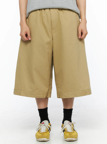 Men's Baggy Bermuda Shorts IL514 Beige front close-up view on model showing elastic drawstring waist, wide-leg silhouette, and cuffed hem with yellow sneakers