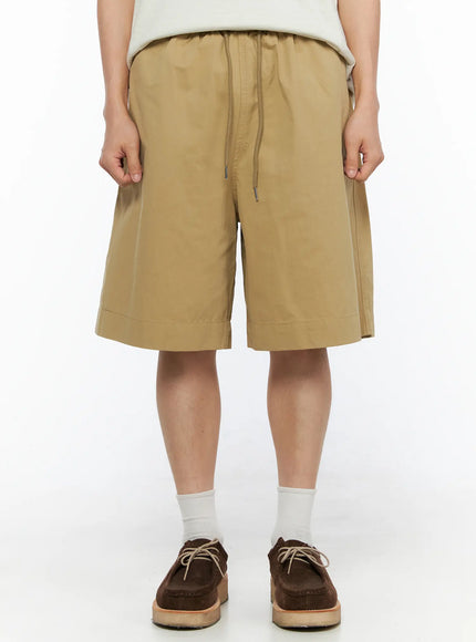 Men's Bermuda Shorts (Beige) IL514 beige close-up front shot on male model showing elastic drawstring waistband and wide-leg silhouette with side seam detail