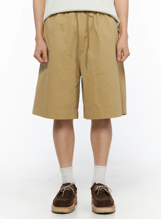 Men's Bermuda Shorts (Beige) IL514 beige close-up front shot on male model showing elastic drawstring waistband and wide-leg silhouette with side seam detail