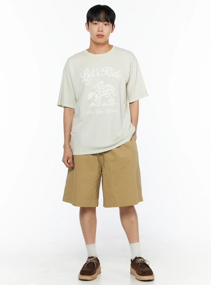 Men's Bermuda Shorts (Beige) IL514 beige full-body front shot on male model with one hand in pocket in relaxed standing pose styled with oversized graphic tee