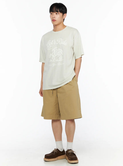 Men's Bermuda Shorts (Beige) IL514 beige three-quarter angle full-body shot on male model with hand in pocket turned slightly showing side profile and wide-leg cut
