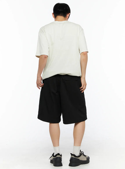 Men's Bermuda Shorts (Black) IL514 black back shot on male model wearing cream graphic tee and chunky sneakers showing back pocket and overall fit