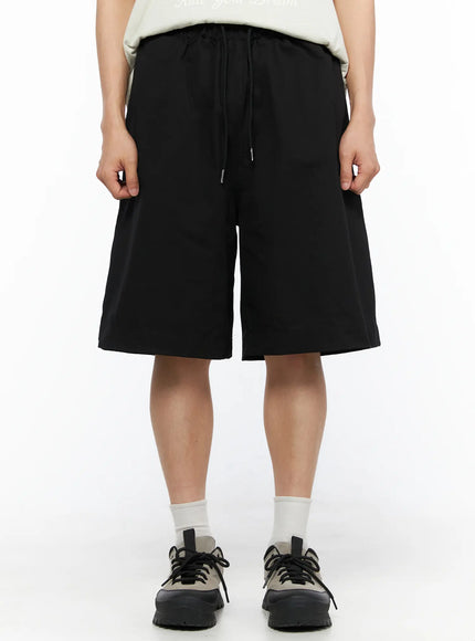LEWKIN Men's Bermuda Shorts (Black) IL514 black front close-up on model showing drawstring elastic waistband and wide-leg silhouette styled with white tee and sneakers