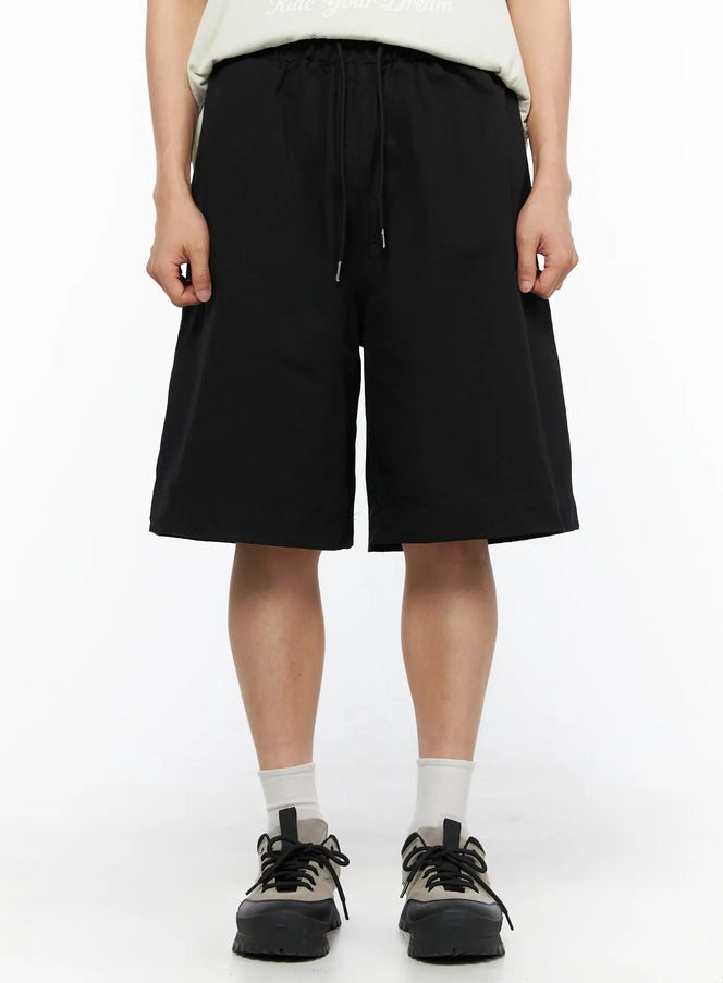 LEWKIN Men's Bermuda Shorts (Black) IL514 black front close-up on model showing drawstring elastic waistband and wide-leg silhouette styled with white tee and sneakers