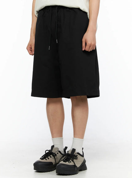 Men's Bermuda Shorts (Black) IL514 black front waist close-up on model highlighting elastic drawstring waistband wide-leg cut and knee-length hem