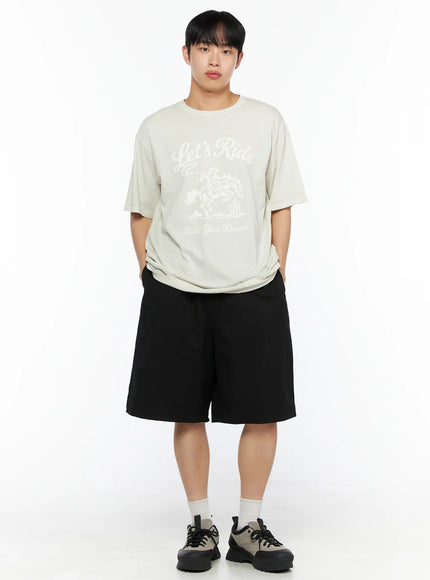 Men's Bermuda Shorts (Black) IL514 black full-body front shot on male model hands in pockets wearing cream graphic tee white socks and grey chunky sneakers