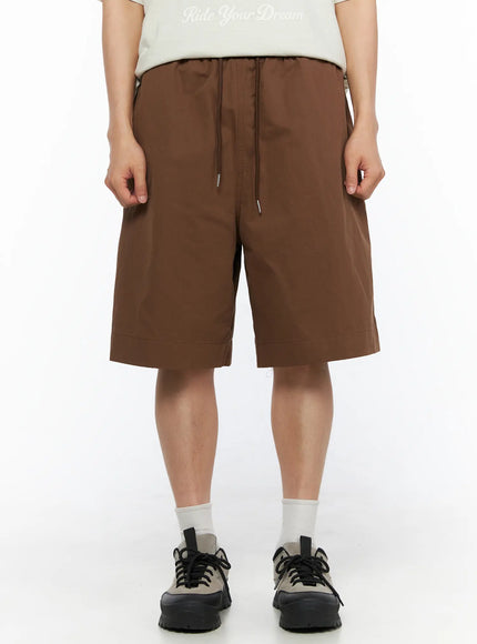 LEWKIN Men's Bermuda Shorts (Dark Brown) IL514 dark brown front view on male model standing straight styled with graphic tee and chunky sneakers