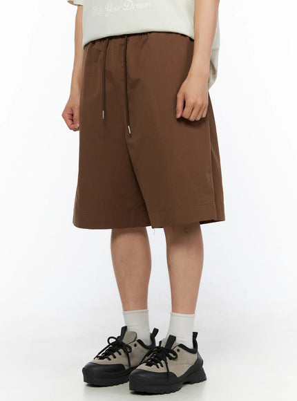 Men's Bermuda Shorts (Dark Brown) IL514 dark brown front three-quarter view on male model showing wide-leg silhouette drawstring waist and sneaker styling