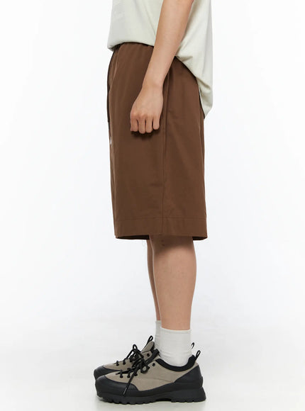 Men's Bermuda Shorts (Dark Brown) IL514 dark brown side view on male model showing clean side seam relaxed fit hem length and chunky sneakers