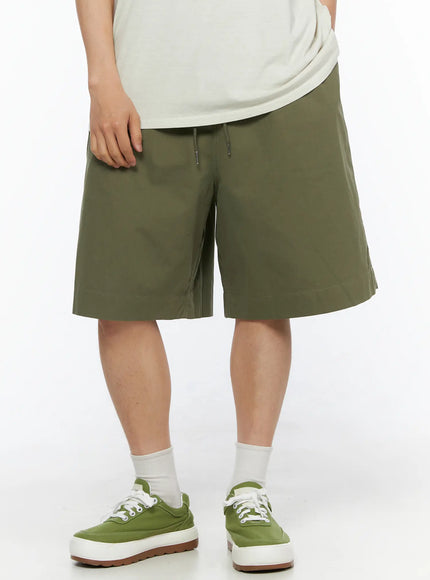 LEWKIN Men's Bermuda Shorts (Dark Green) IL514 Dark green front crop shot on model wearing light tee and green sneakers, drawstring waistband visible