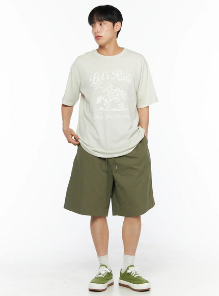 Men's Bermuda Shorts (Dark Green) IL514 Dark green full-body front shot on male model styled with beige graphic tee and green sneakers, angled pose