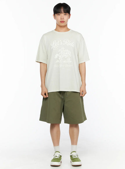 Men's Bermuda Shorts (Dark Green) IL514 Dark green full-body front shot on male model wearing beige graphic tee and green sneakers, standing straight
