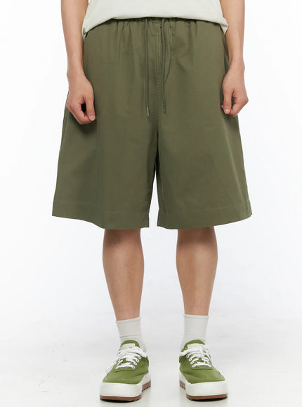 Men's Bermuda Shorts (Dark Green) IL514 Dark green front crop shot on model highlighting elastic drawstring waistband and wide-leg silhouette with green sneakers
