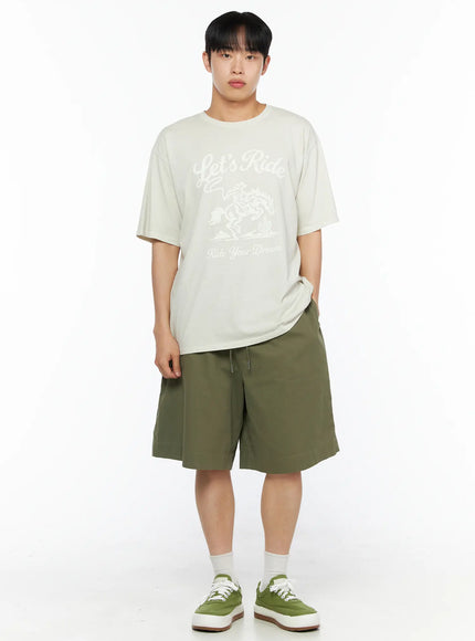 Men's Bermuda Shorts (Dark Green) IL514 Dark green full-body front shot on male model in beige graphic tee, hands in pockets, relaxed wide-leg bermuda fit