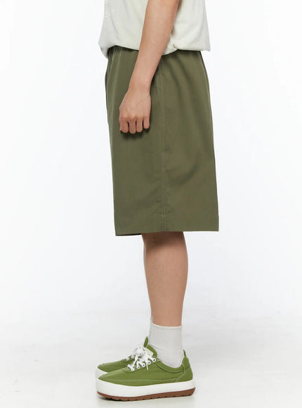 Men's Bermuda Shorts (Dark Green) IL514 Dark green side view on male model in full outfit with beige graphic tee, wide-leg fit and hem detail visible