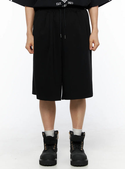 LEWKIN Men's Bermuda Sweat Shorts (Black) IL514 Black M/L front shot on model wearing black graphic tee and boots, wide-leg knee-length silhouette with drawstring waist