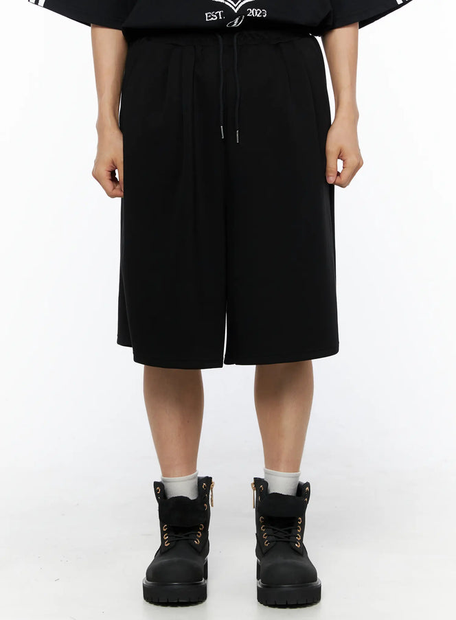 LEWKIN Men's Bermuda Sweat Shorts (Black) IL514 Black M/L front shot on model wearing black graphic tee and boots, wide-leg knee-length silhouette with drawstring waist