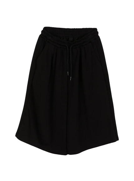 Men's Bermuda Sweat Shorts (Black) IL514 Black flat-lay front view showing elastic drawstring waistband, pleated wide-leg shorts silhouette, and knee-length hem in smooth fabric