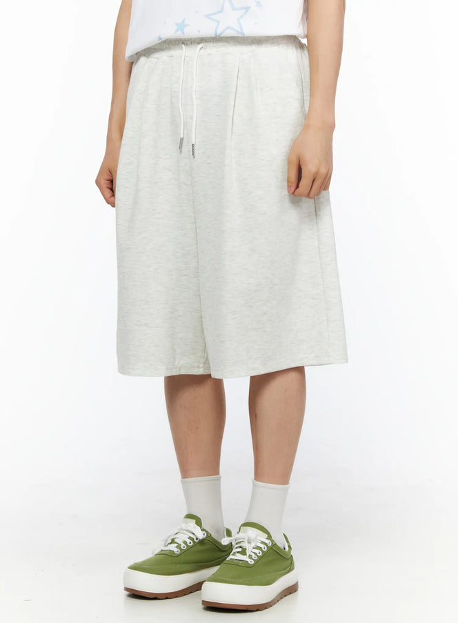Men's Bermuda Sweat Shorts (Light Gray) IL514 Light gray side-angle close-up on model highlighting pleated waist drawstring detail and relaxed silhouette with green sneakers
