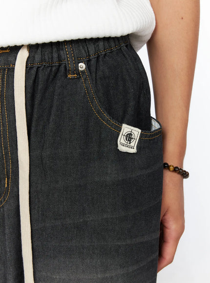 Men's Bryan Drawstring Baggy Jeans IL520 Black close-up detail of elastic waistband, THECROSS woven label patch, gold topstitching on faded denim