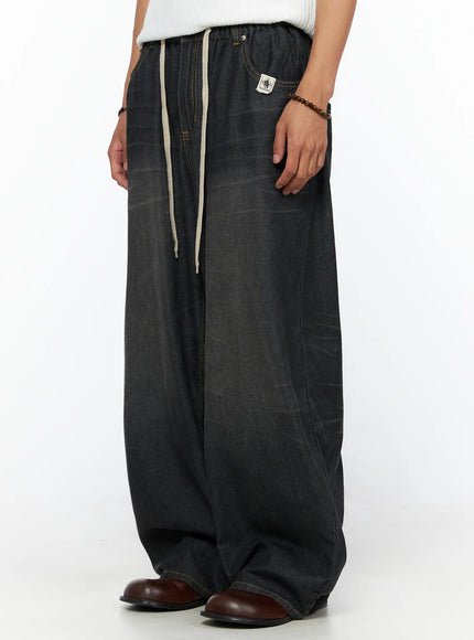 Men's Bryan Drawstring Baggy Jeans IL520 Black side view on model showing cream drawstring, brand patch label, yellow topstitching, ultra-wide leg denim