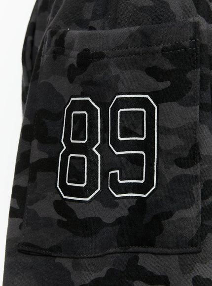 Men's Camo Graphic Shorts (Dark Gray) IL509 Dark gray close-up detail of embroidered 89 numeral patch on back patch pocket with dark camo cotton background