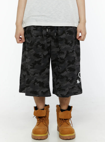 Men's Camo Graphic Shorts (Dark Gray) IL509 Dark gray front view on model, drawstring waist, wide-leg silhouette with star and script logo graphic on hem
