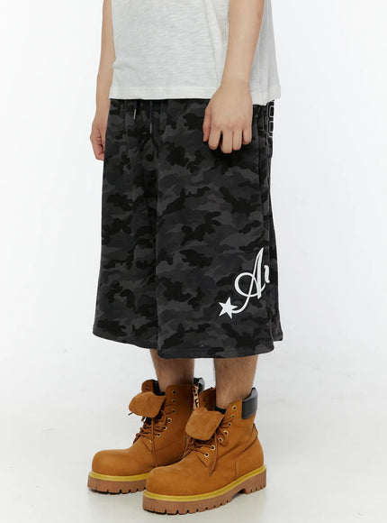 Men's Camo Graphic Shorts (Dark Gray) IL509 Dark gray side view close-up on model showing wide-leg drop crotch silhouette and Angel script graphic on lower leg