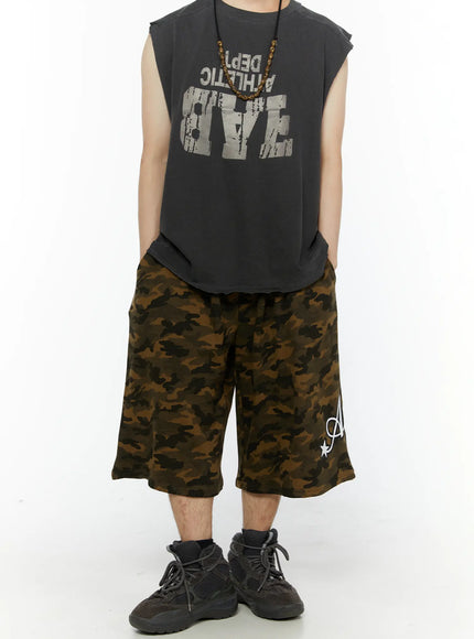 Men's Camo Graphic Shorts (Dark Green) IL509 front full-body on male model standing straight, styled with reversed graphic sleeveless tee and beaded necklace, street style look