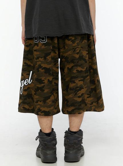 Men's Camo Graphic Shorts (Dark Green) IL509 back view on male model showing 89 patch pocket, wide-leg silhouette, styled with gray sleeveless tee and chunky sneakers
