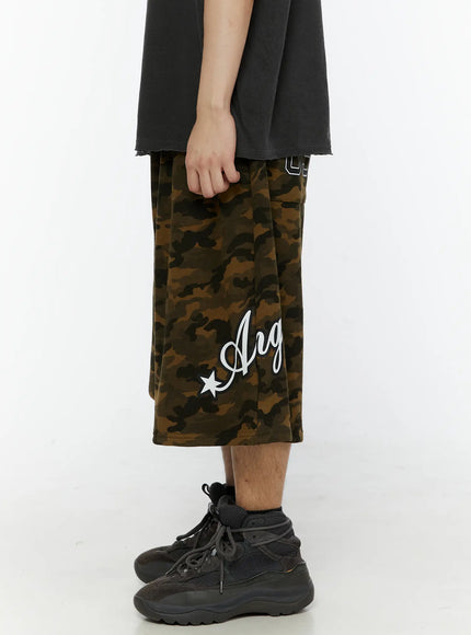 Men's Camo Graphic Shorts (Dark Green) IL509 side close-up on male model showing right leg with Angel script graphic and 89 number patch pocket detail visible at waistband
