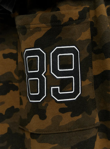 Men's Camo Graphic Shorts (Dark Green) IL509 close-up detail of white Angel script print with star motif on dark green brown camouflage fabric surface