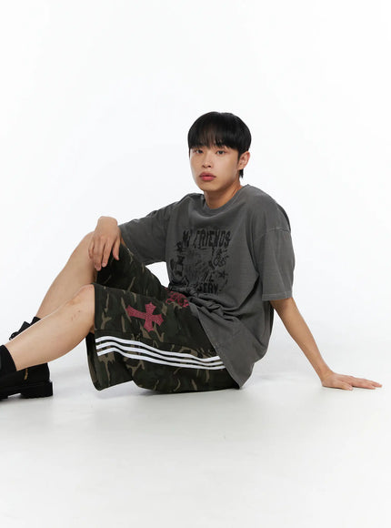 Men's Camo Graphic Sweat Shorts (Dark Green) IL514 Dark green seated model shot styled with grey graphic tee and black boots showing cross and stripe detail