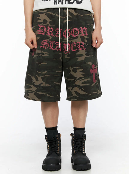 LEWKIN Men's Camo Graphic Sweat Shorts (Dark Green) IL514 Dark green front view on model wearing black boots with pink Dragon Slayer old-english print